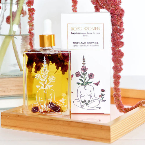 Self-love body oil bottle with decorative packaging on a wooden stand