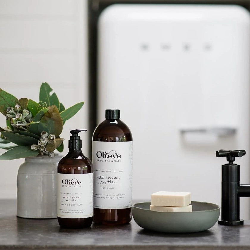 olieve-and-olie-hand-and-body-wash products on a kitchen counter with a vase of greenery and soap.